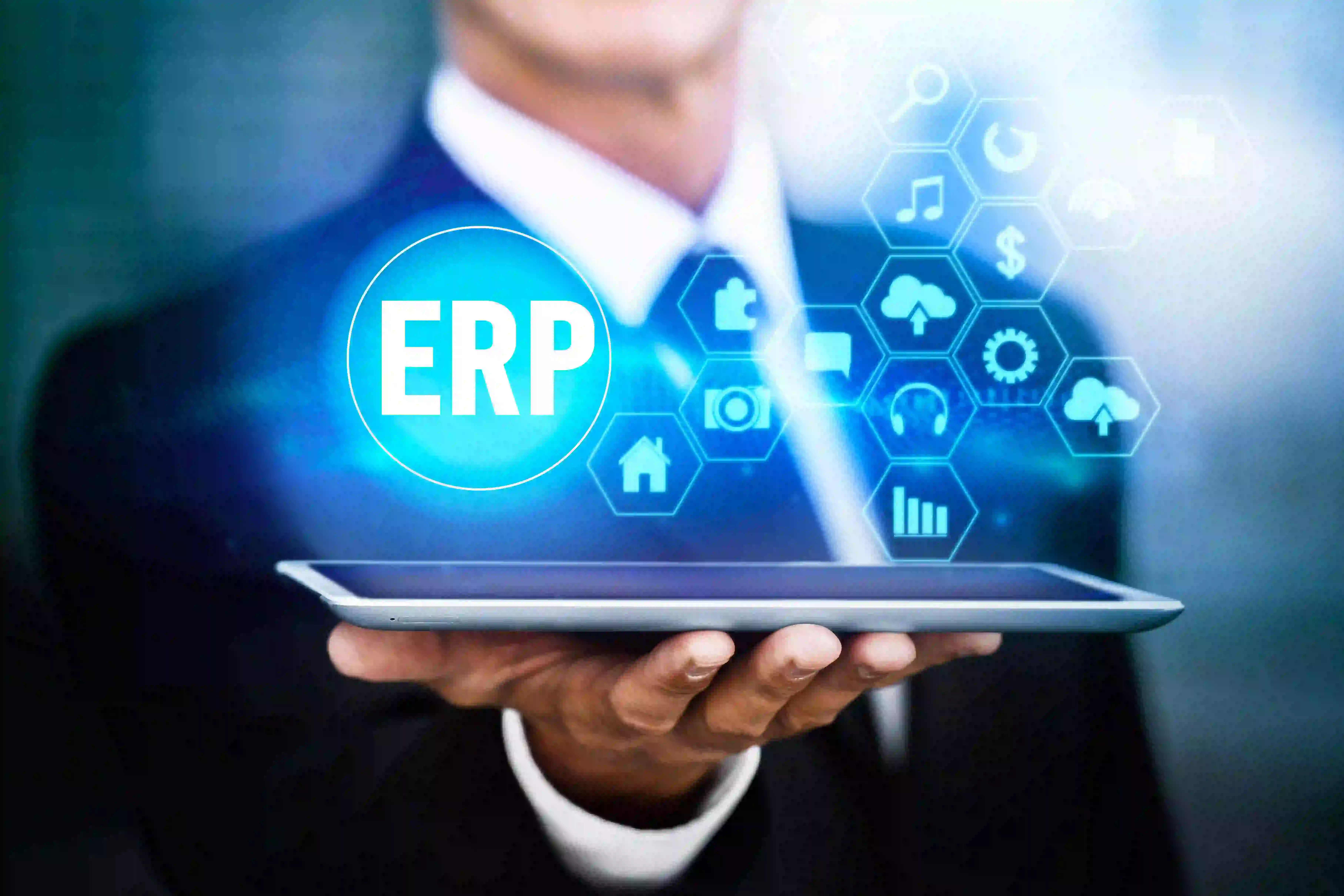 A businessman holds a tablet displaying the word ERP Software Solutions surrounded by digital icons representing various business functions.